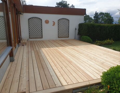 Eine frisch gebaute Holzterrasse in einem Hinterhof, neben einem Haus mit Spalier und Wanddekorationen.