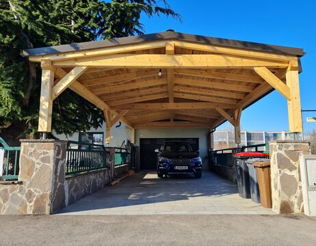 Ein schwarzes Auto, das an einem sonnigen Tag unter einem hölzernen Carport neben einem Haus geparkt ist.