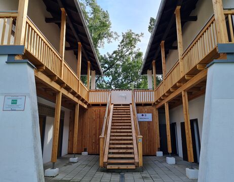 Holztreppe, die zu einem oberen Durchgang zwischen zwei Gebäuden mit Holzgeländern und -pfeilern führt.