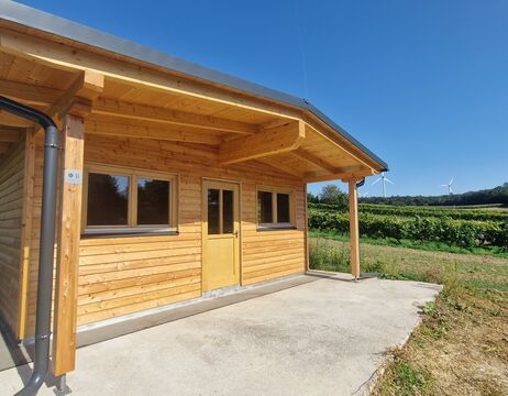 Eine kleine Holzhütte mit einer überdachten Veranda, umgeben von Grün unter einem strahlend blauen Himmel.