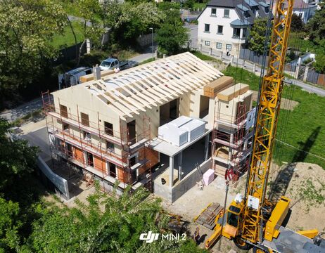Luftaufnahme eines im Bau befindlichen Hauses mit Gerüsten und einem gelben Kran in der Nähe.