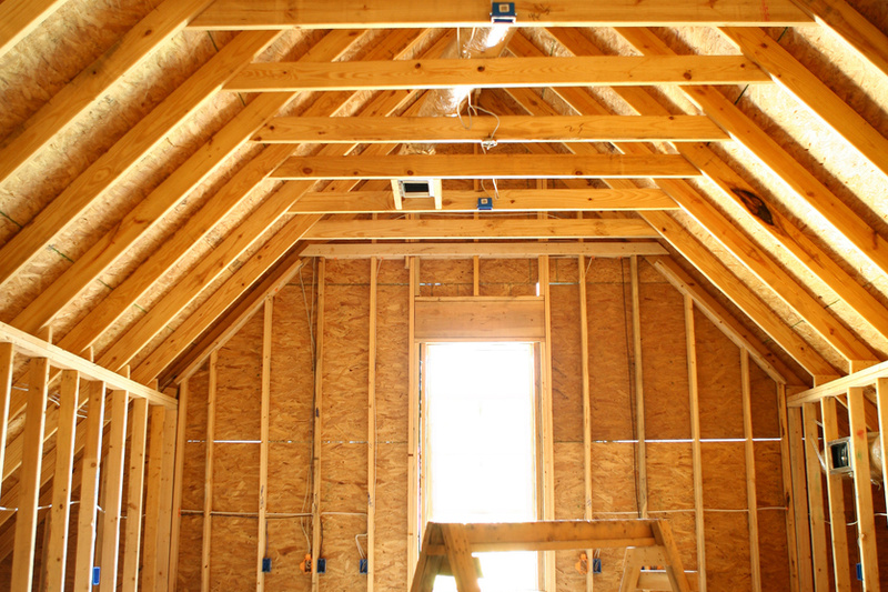 Holzgerüsteter Dachboden mit sichtbaren Dachsparren, Isolierung und einem Fenster, das natürliches Licht hereinlässt.