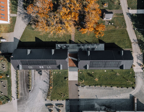 Luftaufnahme eines Gebäudes mit einem Innenhof, umgeben von Gras und Herbstbäumen.