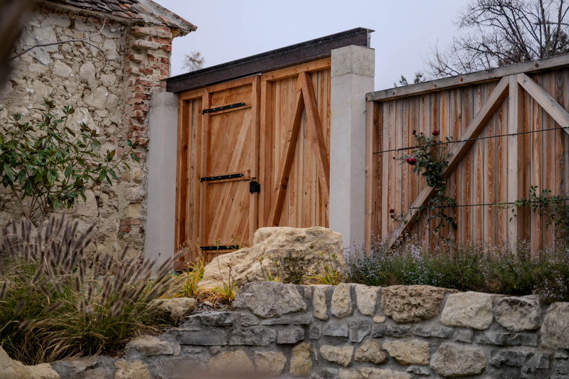 Ein Holztor und ein Zaun mit Steinmauern und Pflanzen in einer rustikalen Gartenumgebung.