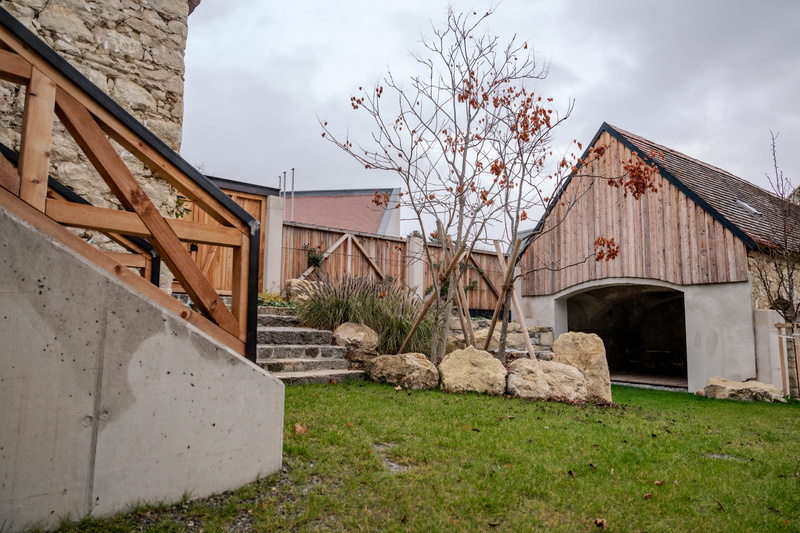 Ein kleiner Hof mit grünem Gras, Steintreppen und modernen Holzgebäuden an einem bewölkten Tag.