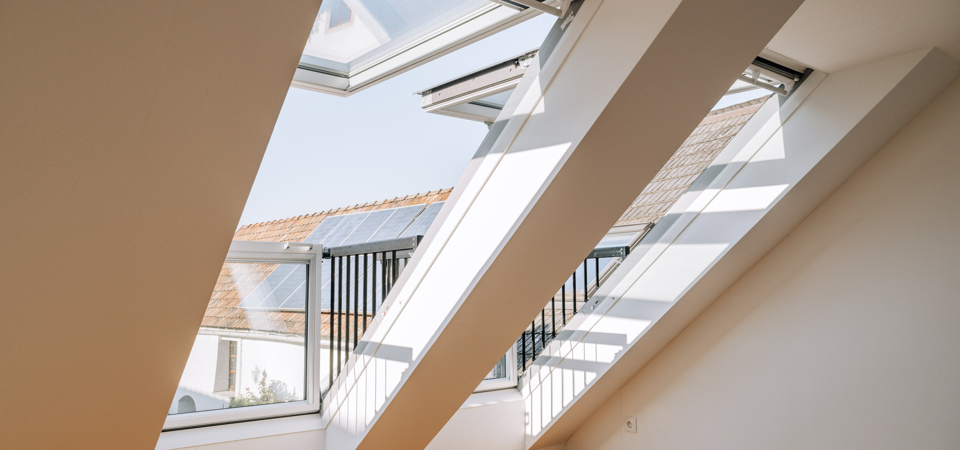 Große Dachfenster geben den Blick auf Dächer mit Sonnenkollektoren frei und lassen das Sonnenlicht in einen hellen Raum.