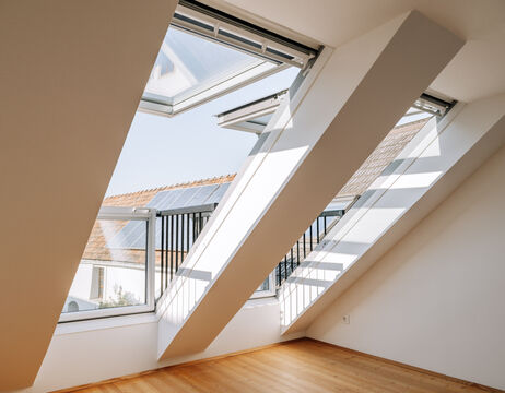 Große Dachfenster geben den Blick auf Dächer mit Sonnenkollektoren frei und lassen das Sonnenlicht in einen hellen Raum.