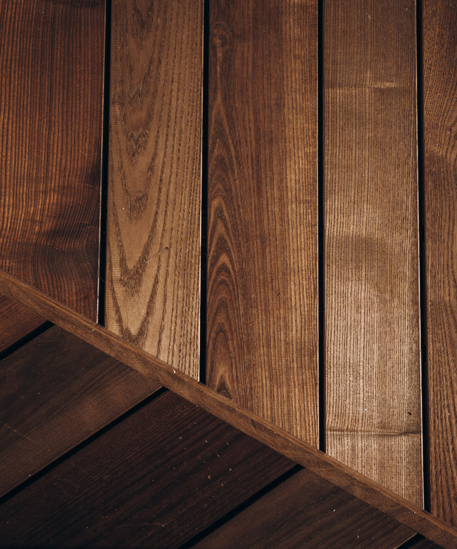 Diagonal und vertikal angeordnete Holzbretter, die unterschiedliche Farbtöne und Holzmaserungen aufweisen.