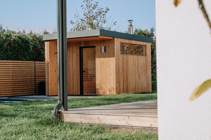 Kleiner moderner Holzschuppen mit Flachdach in einem Hinterhof, umgeben von Gras und einem Holzzaun.
