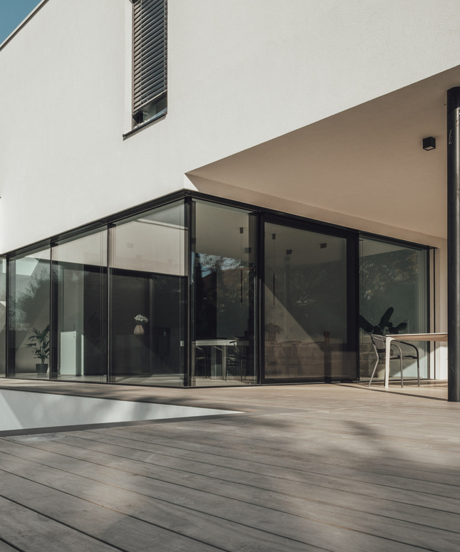Mann in weißem Hemd riecht an einem Glas Wein und steht vor einem großen hölzernen Weinfass.