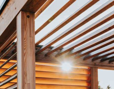 Das Sonnenlicht scheint durch die Holzlatten einer modernen Pergola oder Außenstruktur.