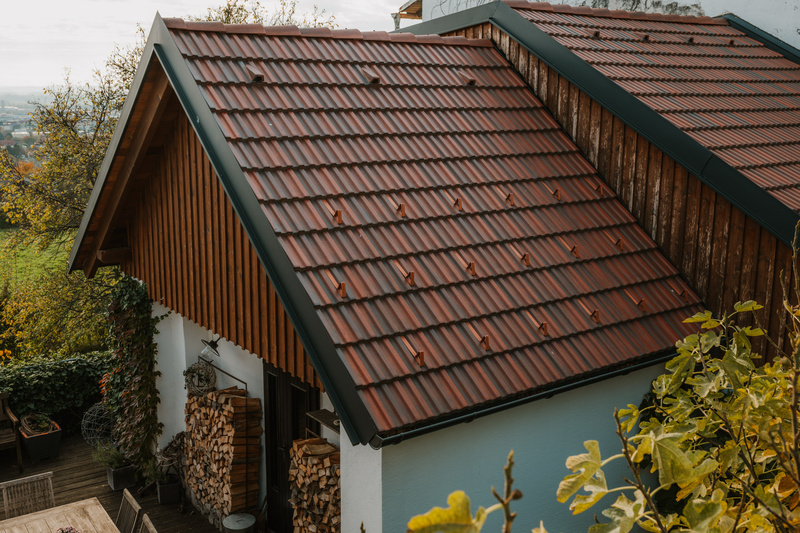 Ein Haus mit einem schrägen roten Ziegeldach, Holzverkleidung und gestapeltem Brennholz neben dem Eingang.