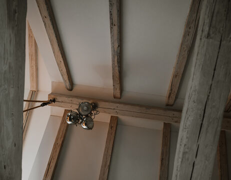 Hölzerne Deckenbalken mit einem von der Decke hängenden Metallkronleuchter, von unten gesehen.