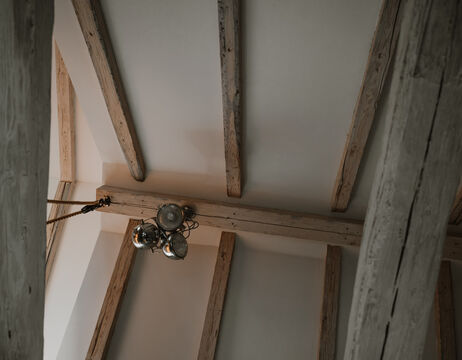 Hölzerne Deckenbalken mit einem von der Decke hängenden Metallkronleuchter.