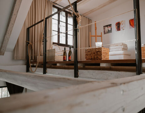 Loft mit großem Fenster, Körben, gefalteten Handtüchern, Weinflaschen und Kunst an der Wand.