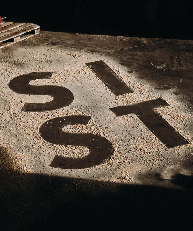 Große Buchstaben mit der Aufschrift SIT sind in einen staubigen Betonboden geschnitten, der von einem Sonnenstrahl beleuchtet wird.