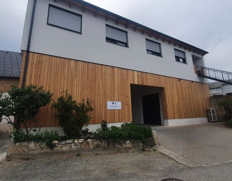 Ein modernes, zweistöckiges Gebäude mit Holzvertäfelung und einer zentralen, offenen Garage unter einem bewölkten Himmel.