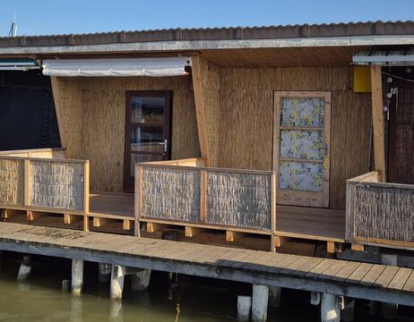 Ein Holzhaus auf Stelzen über dem Wasser mit einer Veranda und einer mit gemustertem Papier überzogenen Tür.