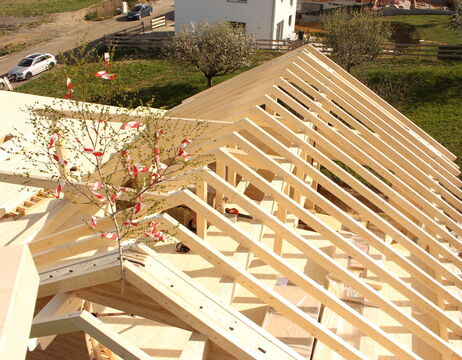 Ein teilweise aufgebautes Holzdach mit einem kleinen geschmückten Baum darauf, im Freien an einem sonnigen Tag.