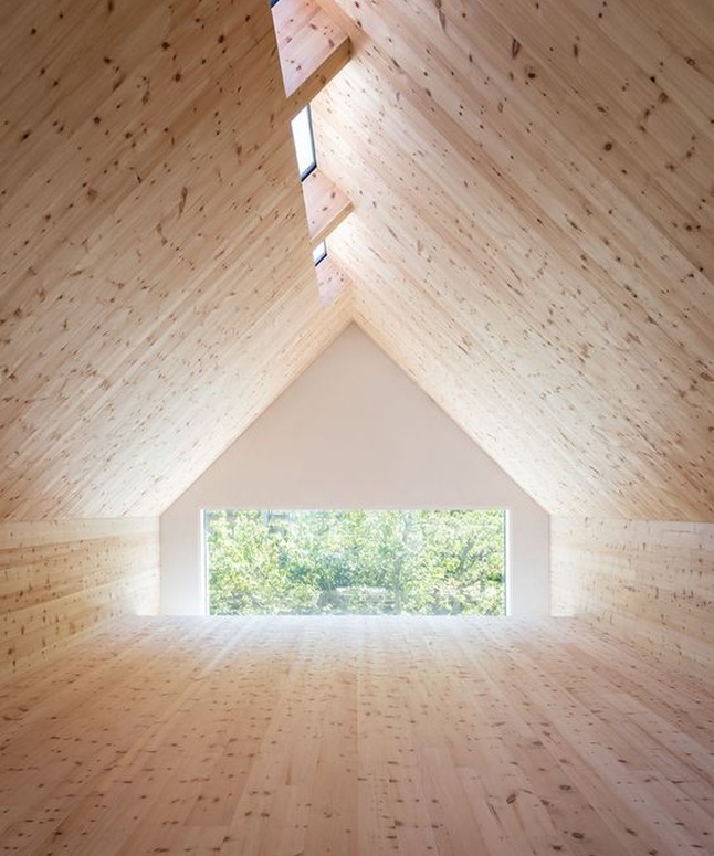 Ein geräumiger hölzerner Dachboden mit einer dreieckigen Decke, Oberlichtern und einem großen Fenster mit Blick ins Grüne.
