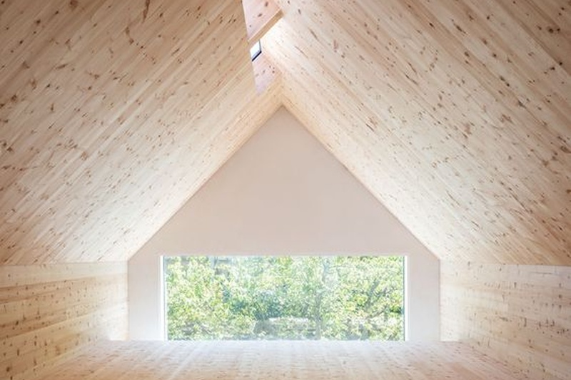 Ein geräumiger hölzerner Dachboden mit einer dreieckigen Decke, Oberlichtern und einem großen Fenster mit Blick ins Grüne.