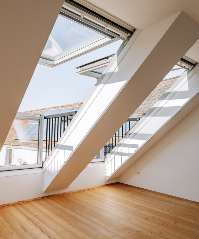 Helles Dachgeschoss mit großen Dachflächenfenstern, schrägen Balken und hellem Holzboden.