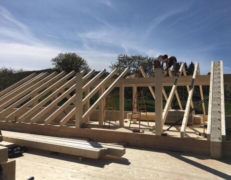 Zwei Personen arbeiten an einem sonnigen Tag am Holzrahmen eines im Bau befindlichen Hauses.