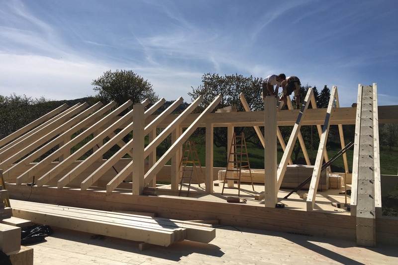 Zwei Personen arbeiten an einem sonnigen Tag am Holzrahmen eines im Bau befindlichen Hauses.