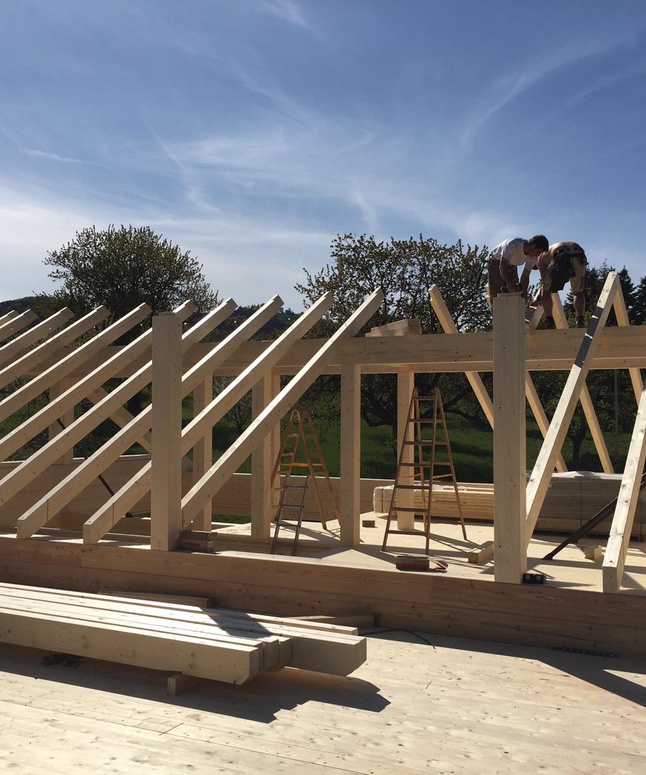Zwei Personen arbeiten an einem sonnigen Tag am Holzrahmen eines im Bau befindlichen Hauses.
