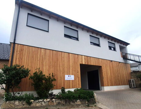 Modernes zweistöckiges Gebäude mit Holzverkleidung, drei Fenstern und einer offenen Garageneinfahrt im Erdgeschoss.