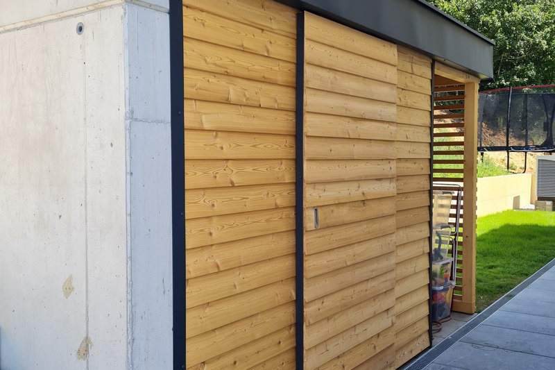 Modernes Gebäude mit heller Holzverkleidung und Betonmauer neben einer grünen Wiese.