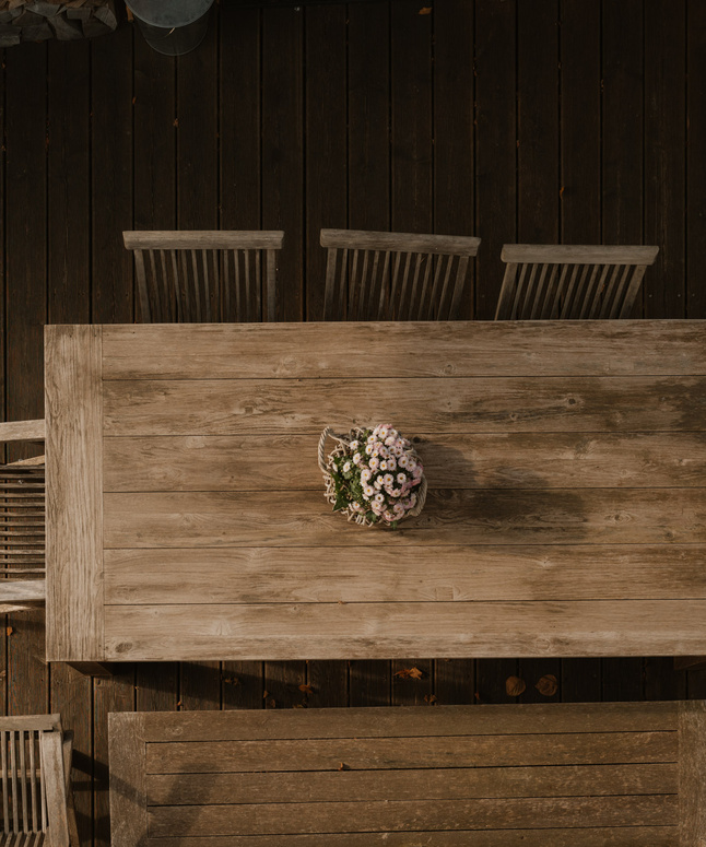 Ein Holztisch mit einem Blumenarrangement, umgeben von fünf Stühlen, von oben gesehen.