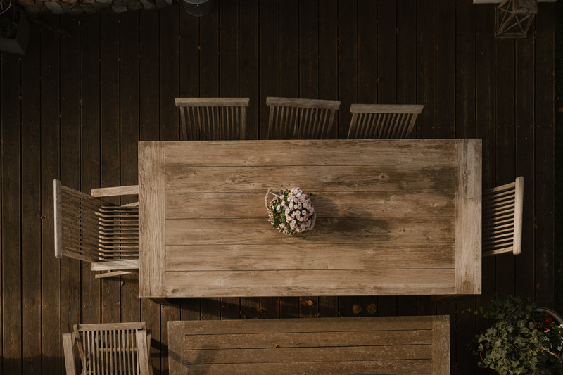 Ein Holztisch mit einem Blumenarrangement, umgeben von fünf Stühlen, von oben gesehen.