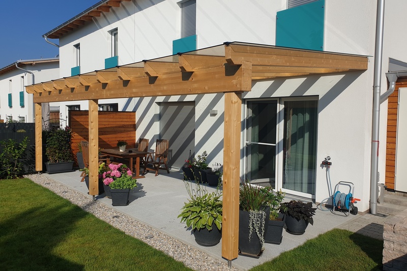Modernes Haus mit einer hölzernen Pergola über einem Innenhof, umgeben von Topfpflanzen, Stühlen und einem Tisch.