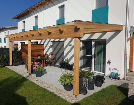 Modernes Haus mit einer hölzernen Pergola über einem Innenhof, umgeben von Topfpflanzen, Stühlen und einem Tisch.
