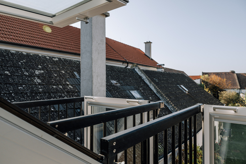 Blick von einem Balkon mit offenen Glastüren auf die Dächer unter einem klaren blauen Himmel.