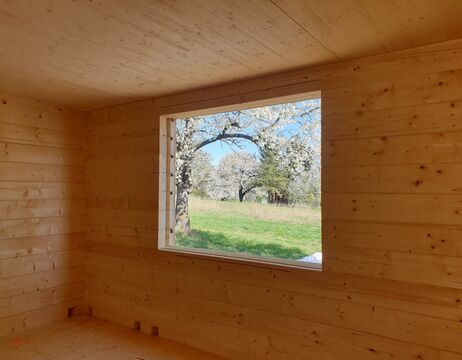 Ein hölzernes Zimmer mit einem großen Fenster mit Blick auf grünes Gras und blühende Bäume draußen.