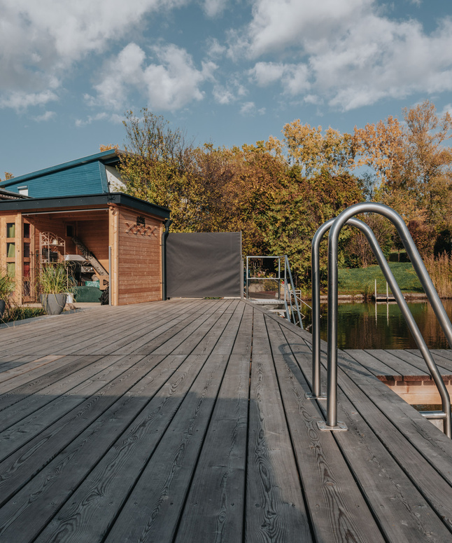 Eine lächelnde Frau in traditioneller Kleidung hält ein Tablett mit Gläsern und einer Karaffe in einem rustikalen Restaurant.