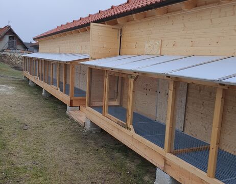 Tiergehege aus Holz mit Maschendrahtfronten, die an einem Gebäude befestigt sind und außen auf Zementblöcken stehen.