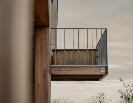 Ein moderner, an einem Gebäude angebrachter Balkon aus Holz und Metall, von der Seite gegen einen bewölkten Himmel fotografiert.