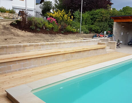 Holzterrasse und Steinbank neben einem Swimmingpool, mit Garten und Haus im Hintergrund.