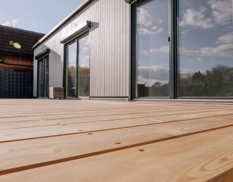 Niedriger Blickwinkel auf ein modernes Haus mit großen Glastüren und einer Holzterrasse unter einem teilweise bewölkten Himmel.