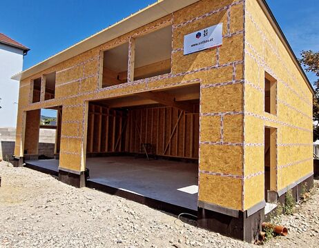 Ein im Bau befindliches Haus mit freiliegendem Holzgerüst und großen offenen Garagentoren.