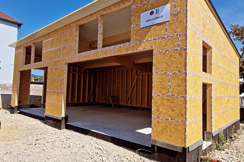 Ein im Bau befindliches Haus mit freiliegendem Holzgerüst und großen offenen Garagentoren.