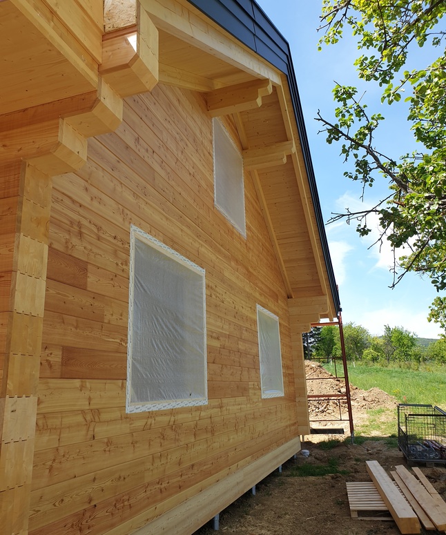 Ein neu gebautes Holzhaus mit kunststoffverkleideten Fenstern und einem blauen Himmel im Hintergrund.