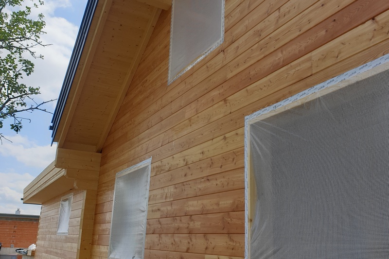 Außenansicht eines Holzhauses mit Fenstern, die mit einem Schutzgitter abgedeckt sind und an einem sonnigen Tag gestrichen oder versiegelt werden können.