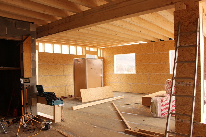 Ein teilweise gebauter Raum mit freiliegenden Holzbalken, Isolierung und verstreutem Baumaterial.