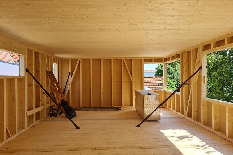 Unfertiger Holzraum im Bau mit offenen Fenstern und Baumaterialien im Inneren.