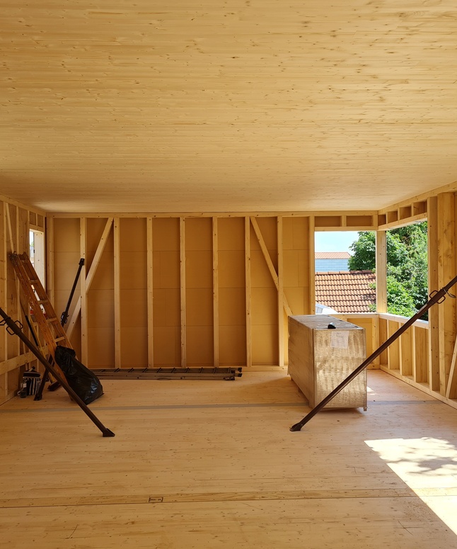 Unfertiger Holzraum im Bau mit offenen Fenstern und Baumaterialien im Inneren.