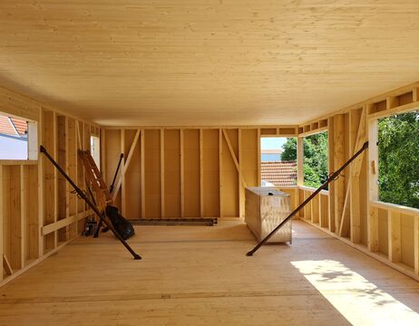 Unfertiger Holzraum im Bau mit offenen Fenstern und Baumaterialien im Inneren.